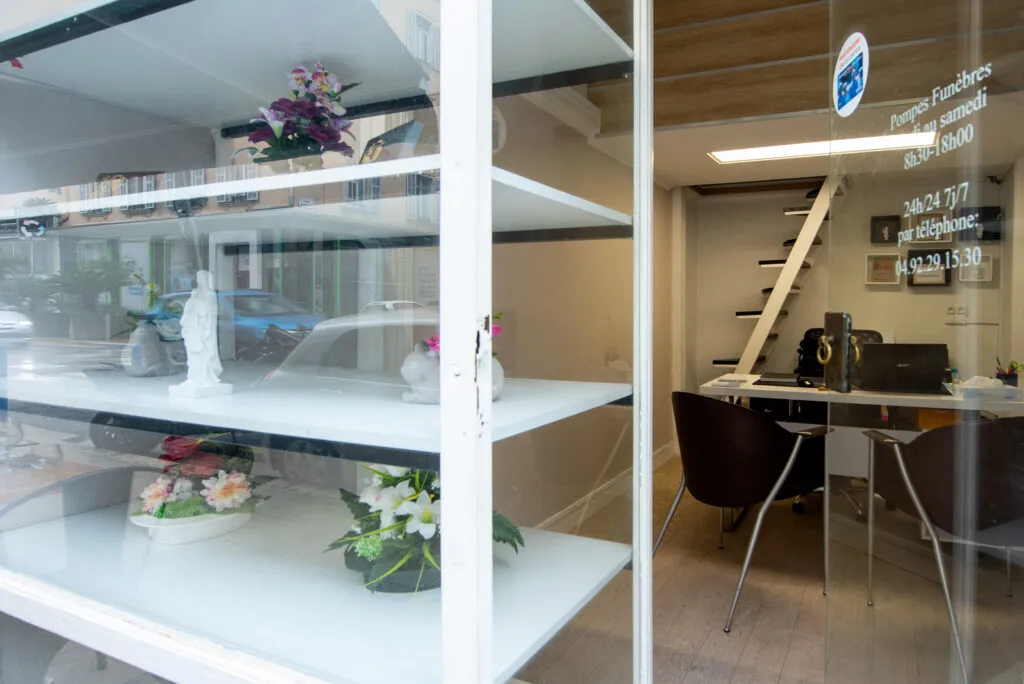 Vitrine d'exposition avec compositions florales et vue sur l'espace d'accueil de l'agence